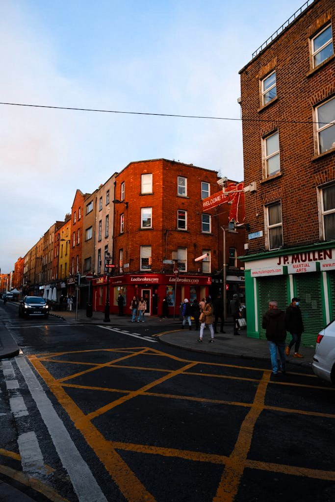 A bustling city street with pedestrians, cars, and urban buildings at sunset.